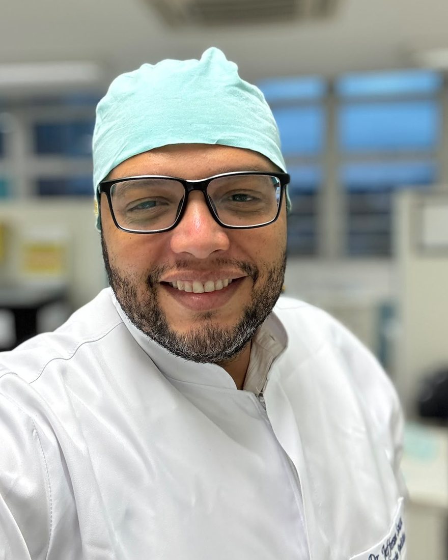 Dentista Jefferson Souza de jaleco e touca no consultório